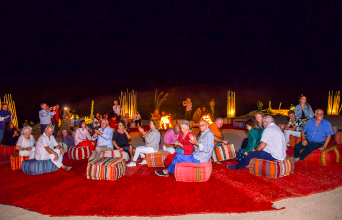 Group of people seated on colorful cushions at a nighttime outdoor gathering in Agafay desert camp.