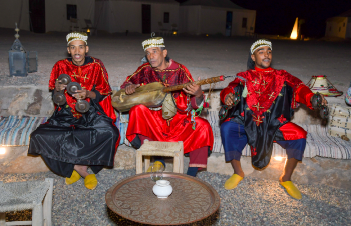 Three musicians in traditional attire performing at a camp in Agafay.