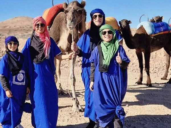 A family dressed in traditional blue attire posing with camels in the Agafay Desert