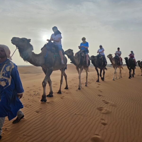 Tourists riding camels led by a guide in traditional attire through the desert.